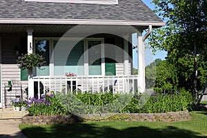 Front of house, porch and flower garden with purple Irises, Purple Pansies and a hanging basket in the summer