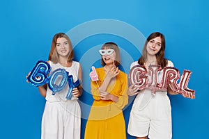 Front image of a three of happy women to have gender reveals envent, isolated blue background.