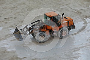 front loader with small wheels against the background of a large pile of stone sand and a blue sky with white clouds. Side view