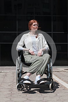 In front of a modern corporate building, a young woman sitting in a wheelchair confidently, symbolizing empowerment