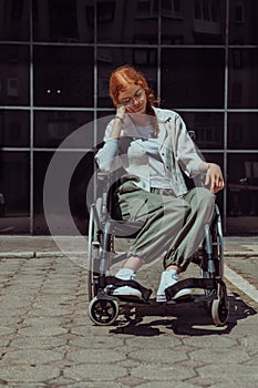 In front of a modern corporate building, a young woman sitting in a wheelchair confidently, symbolizing empowerment