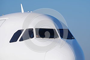 The front nose and cockpit of an Airbus A319-100 passenger plane, the cockpit glazing, blue sky in the background