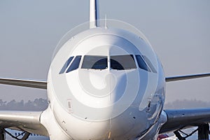 The front nose and cockpit of an Airbus A319-100 passenger plane, the cockpit glazing, blue sky in the background