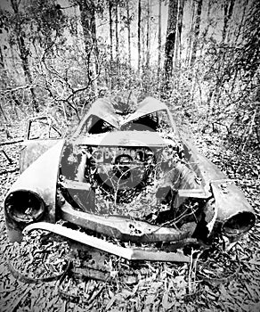 Front of old wrecked car missing the hood buried in the deep woods