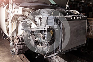 The front part of the car after an accident in a car repair service with a disassembled hood and metal grille and various parts in