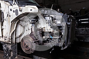 The front part of the car after an accident in a car repair service with a disassembled hood and metal grille and various parts in