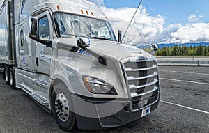 The front passenger side of a white Freightliner Cascadia semi truck parked in a rest stop on Interstate 90 in Washington, USA