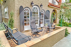 Front patio of house with bench and chairs against arched windows with shutters