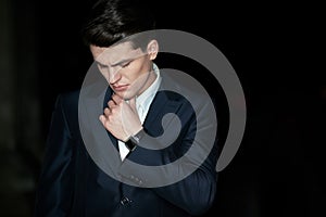 Front portrait of a businessman posing with crossed arms in suit, wear watch on his hand, isolated black background.