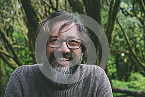 Front portrait of happy and cheerful mature man smiling and looking on camera with green forest woods in background. People