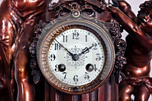 A front portrait of the retro clock face of an old vintage clock made of wood and metal with beautiful clock hands and numbers for