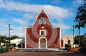 Front of the red colonial church Itzimna in a park with trees, Merida, Yucatan, Mexico photo