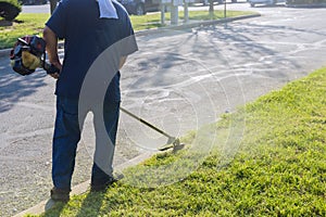 In front of road, a municipal worker lawn mower mows fresh green grass with hand mower