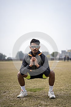 Front shot of an indian boy doing squats in the field wearing sports outfit. Sports and lifestyle concept