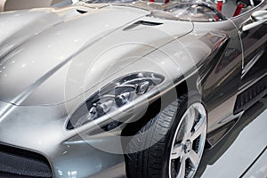 Front, side, close up view of hood, left headlight, mirror, chrome wheel disc of modern roofless grey sport coupe car