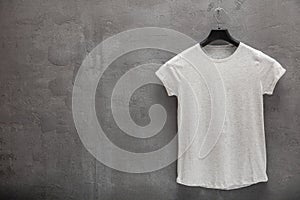 Front side of female grey melange cotton t-shirt on a hanger and a concrete wall in the background