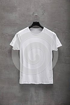 Front side of male white cotton t-shirt on a hanger and a concrete wall in the background