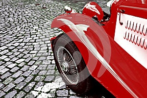 Front side part of vintage classic red hot rod car on a cobble road