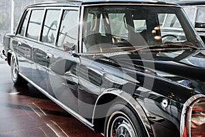 Front and side view of black retro business class limousine with right headlight, chrome mirror and wheel arch on brown