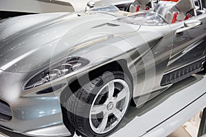 Front, side view of left headlight, mirror, chrome wheel disc of modern roofless grey sport coupe car