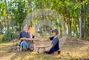Front and side view of senior Asian woman with traditional clothes winnow rice using basketry and little girl stay beside and also