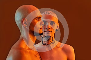 Front and side view of young half naked twin brothers with tattoos and piercings posing together, standing isolated over