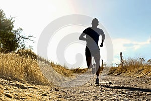 Front silhouette young sport man running cross country workout at summer sunset