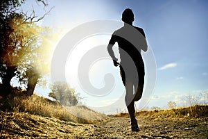 Front silhouette young sport man running cross country workout at summer sunset