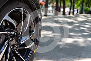The front of the sports car. Wheel of a sports car on the background of a blurred sidewalk in a trendy metropolis area. Sports Car