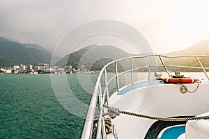 Front of travel boat with lifebuoy and golden light over Sun Moon Lake with mountain and town in background in Yuchi Township.