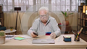 In front of tue camera old man good looking concentrated order something online from the smartphone using the credit