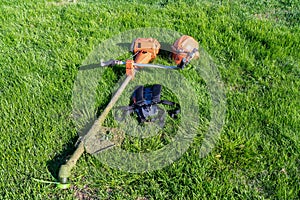 Front up view at handheld gasoline lawn mower, safety helmet with eye and hearing protection, padded shoulder straps left after