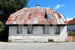 Front view of abandoned small urban family house on cracked stone and concrete foundation with rusted metal roof tiles