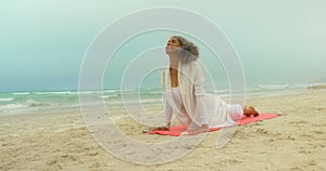 Front view of active senior African American woman doing yoga on exercise mat at the beach 4k