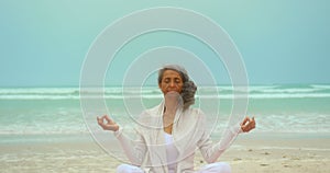 Front view of active senior African American woman doing yoga on exercise mat at the beach 4k