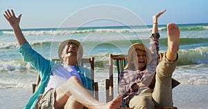 Front view of active senior Caucasian couple having fun on a sun lounger at beach 4k