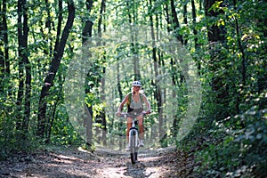 Front view of active senior woman biker cycling outdoors in forest.