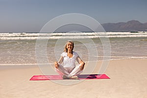 Front view of senior woman meditating at beach on a sunny day