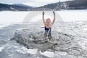 Front view of active senior woman in swimsuit splashing water outdoors in winter, cold therapy concept.