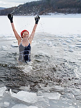 Front view of active senior woman in swimsuit splashing water outdoors in winter, cold therapy concept.