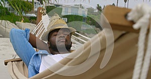 Front view of African american man sleeping in a hammock on the beach 4k