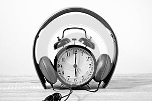 Front View Alarm Clock put on headphones over Wooden Table. Time