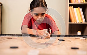 Front view of alone Young girl kid practicing or playing Carrom board at home - Concept of autism and introvert.