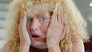 Front view of an anxious young curly redhead woman watching a horror movie attentively, having a feeling of fright and