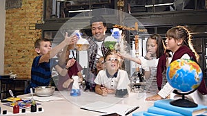 Front view. Asian male science teacher teaching young students doing chermical experiment, holding two flasks with