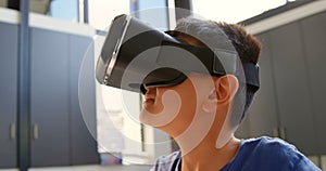 Front view of Asian schoolboy sitting at desk and using virtual reality headset in classroom 4k