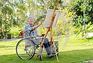 Front view of Asian senior man sit on wheelchair and paint the painting outdoor for relax and revive good health of old people