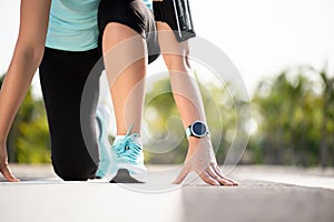 Front view of athletic women in running start pose on running track in the garden street. Sport and running concept