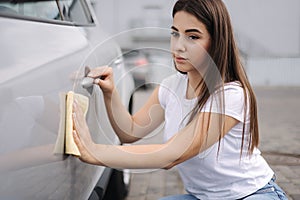 Front view of attractive happy joyful female driver washing her car with special rag in self-service car wash