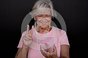 Front view of attractive senior woman smiling on social media with smart phone, on black background